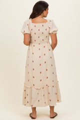 woman wearing a beige maternity dress with floral embroidery and a ruffled hem, seen from the back