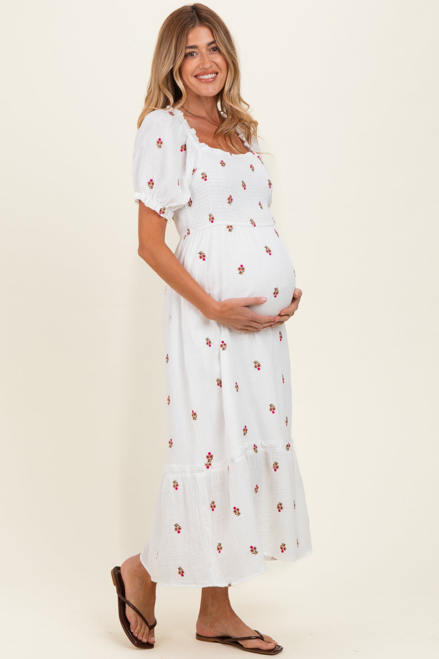 woman wearing a white maternity dress with floral print and puff sleeves, cradling her baby bump