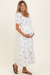 woman wearing a white maternity dress with floral print and puff sleeves, cradling her baby bump