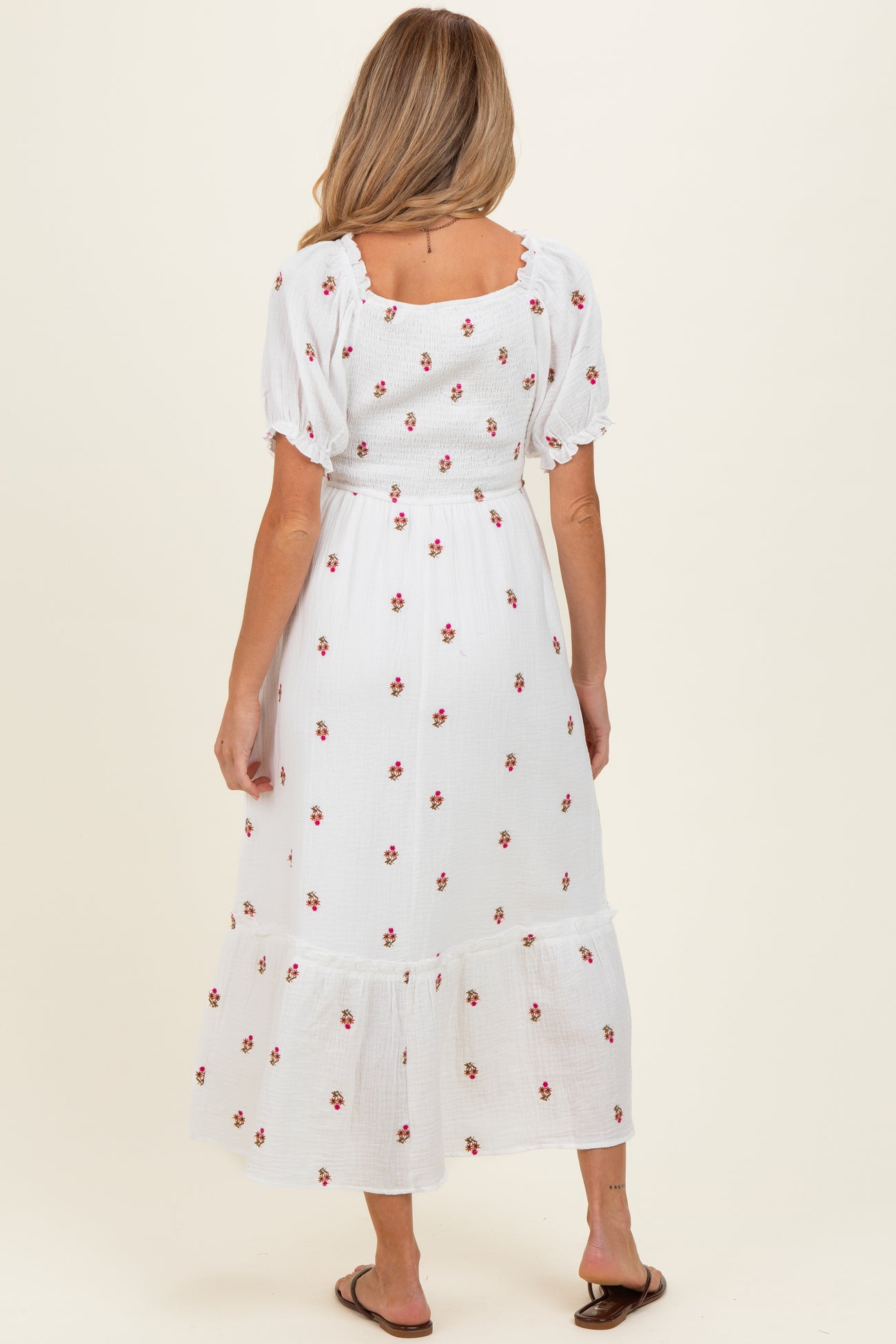 woman wearing a white floral maternity maxi dress with puff sleeves and ruffled hem, showing a baby bump from the back