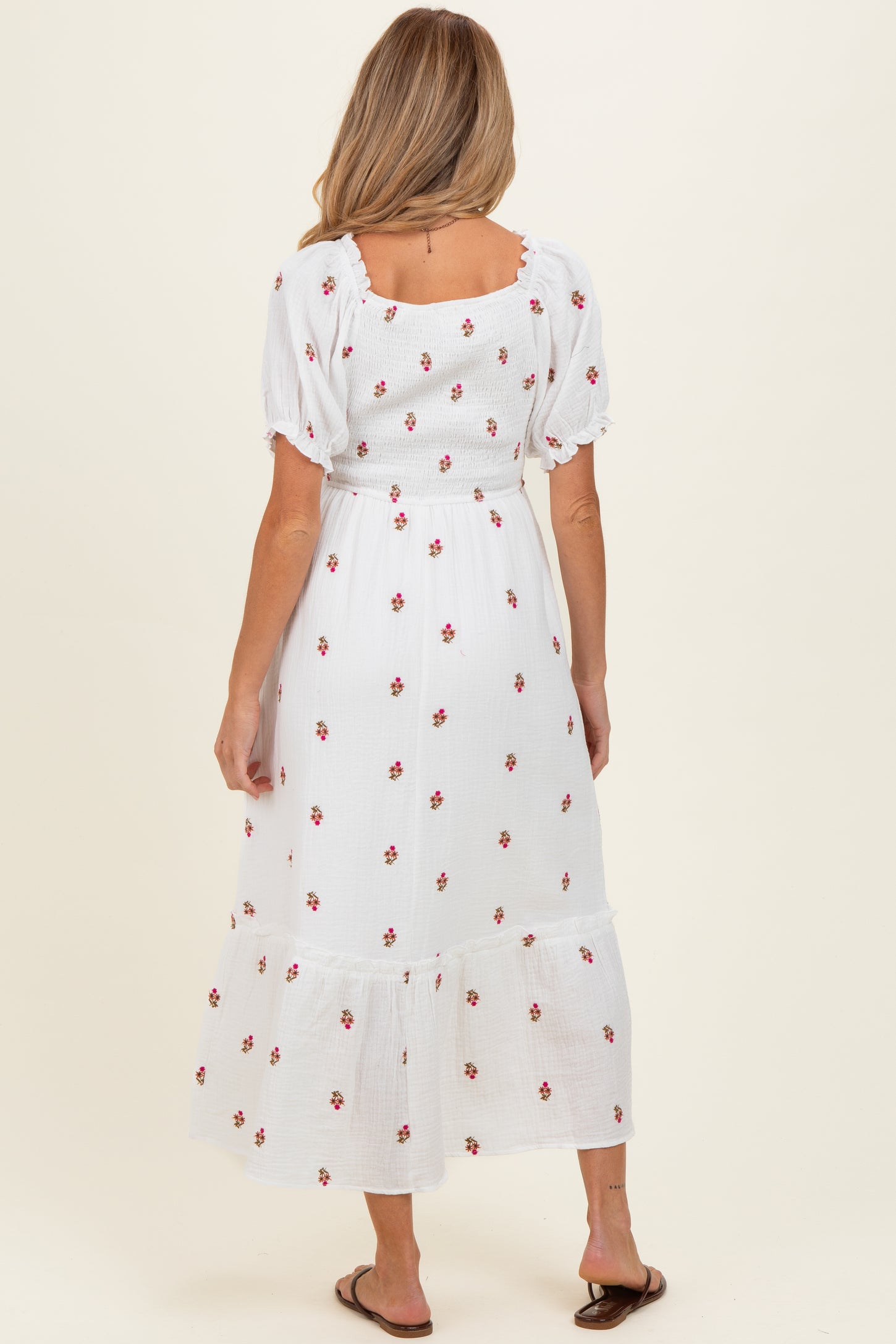 woman wearing a white floral maternity maxi dress with puff sleeves and ruffled hem, showing a baby bump from the back