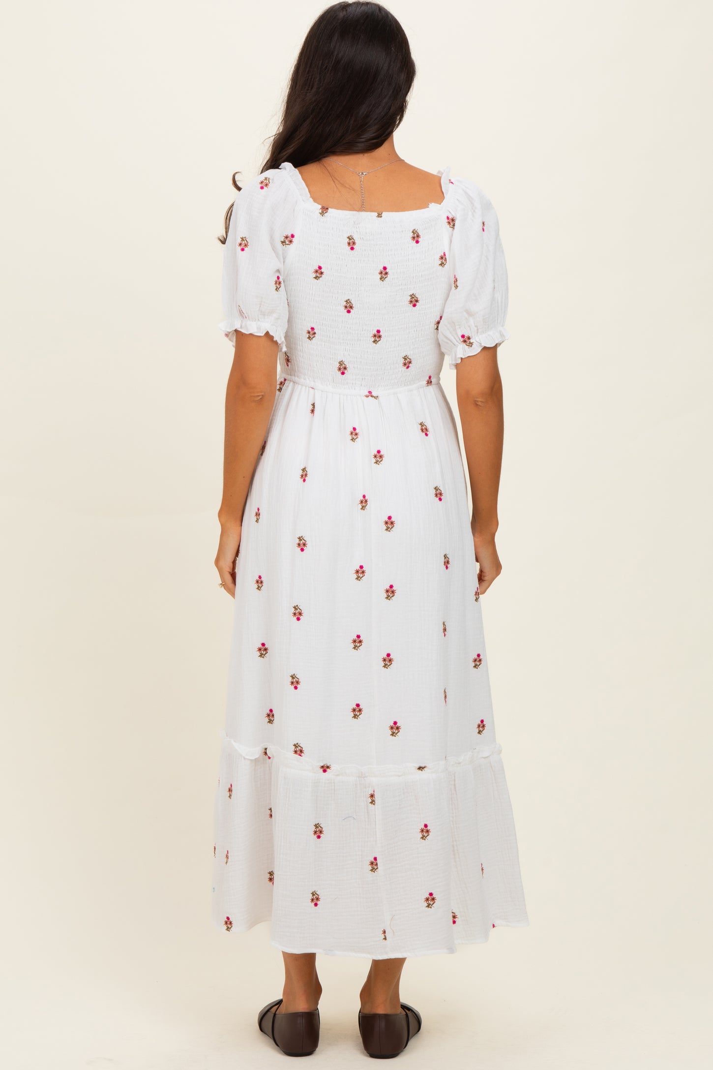 woman wearing a white floral maxi dress with puff sleeves and a tiered skirt, standing with her back to the camera