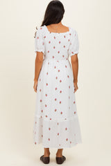 woman wearing a white floral maxi dress with puff sleeves and a tiered skirt, standing with her back to the camera
