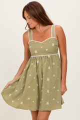 woman wearing a green sleeveless dress with embroidery and lace trim, gently swaying the skirt