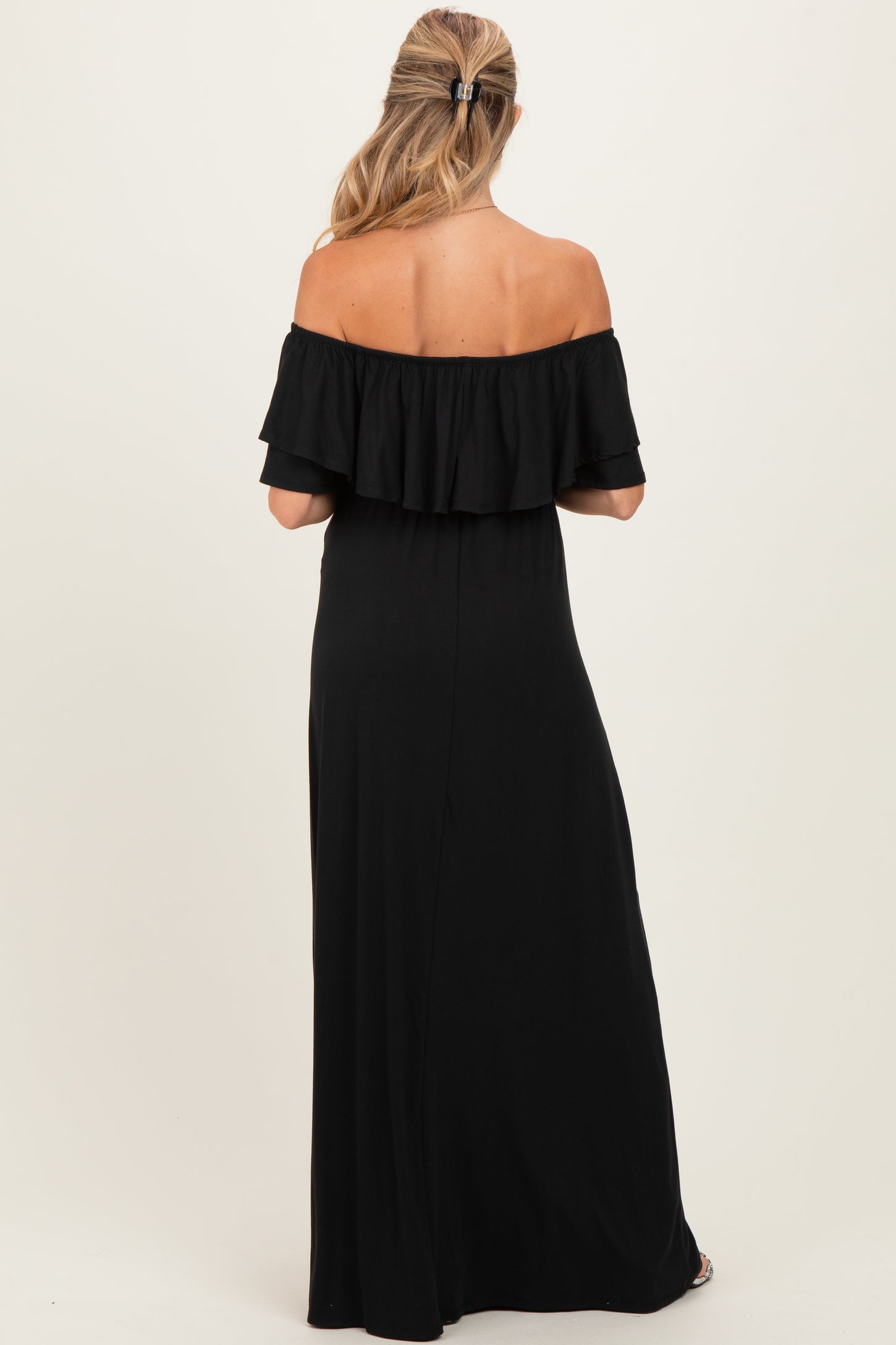 woman wearing a black off-the-shoulder maternity maxi dress, showing the ruffled neckline from the back