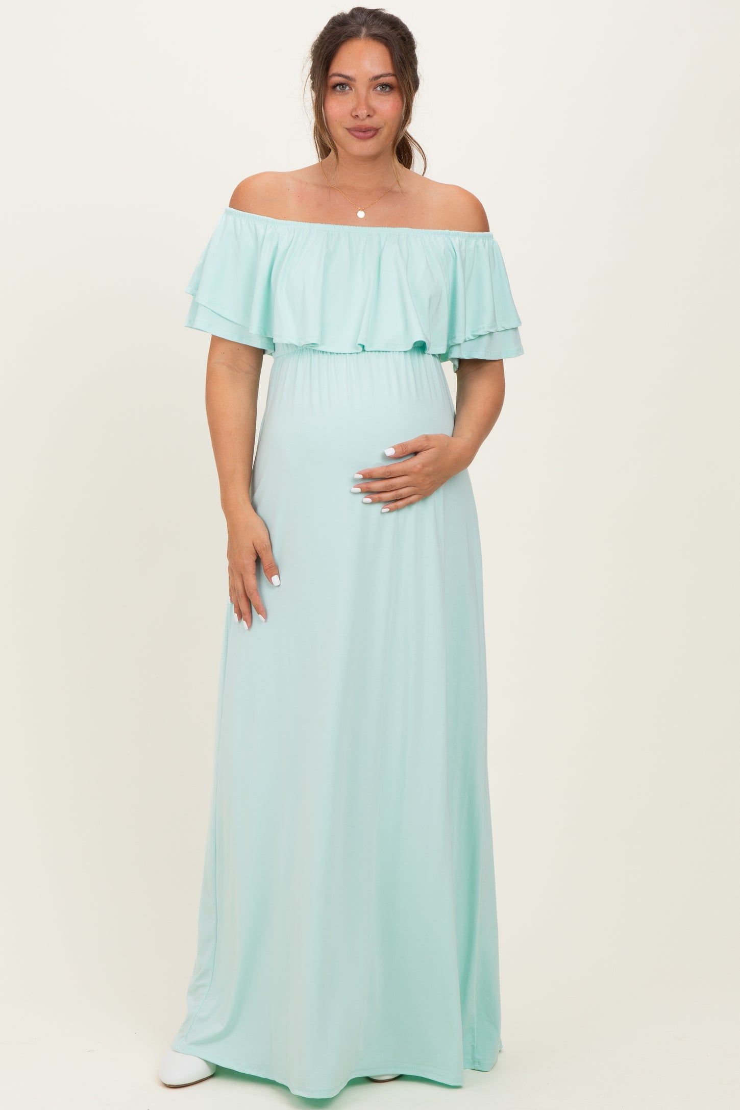 woman wearing a light mint green off-the-shoulder maternity dress with ruffle details and holding her baby bump