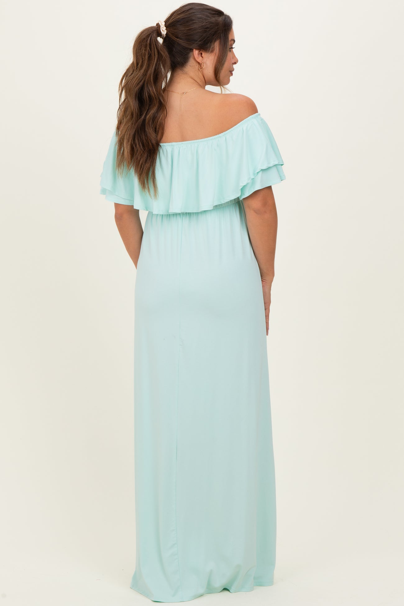 woman wearing a mint green off-the-shoulder maternity maxi dress with ruffle details and an elastic waistband