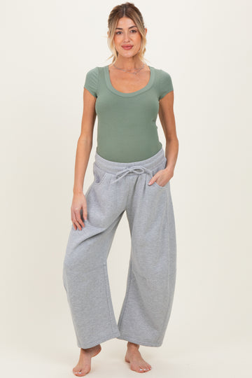 woman wearing a green ribbed short sleeve maternity top and gray wide-leg pants, showcasing a visible baby bump