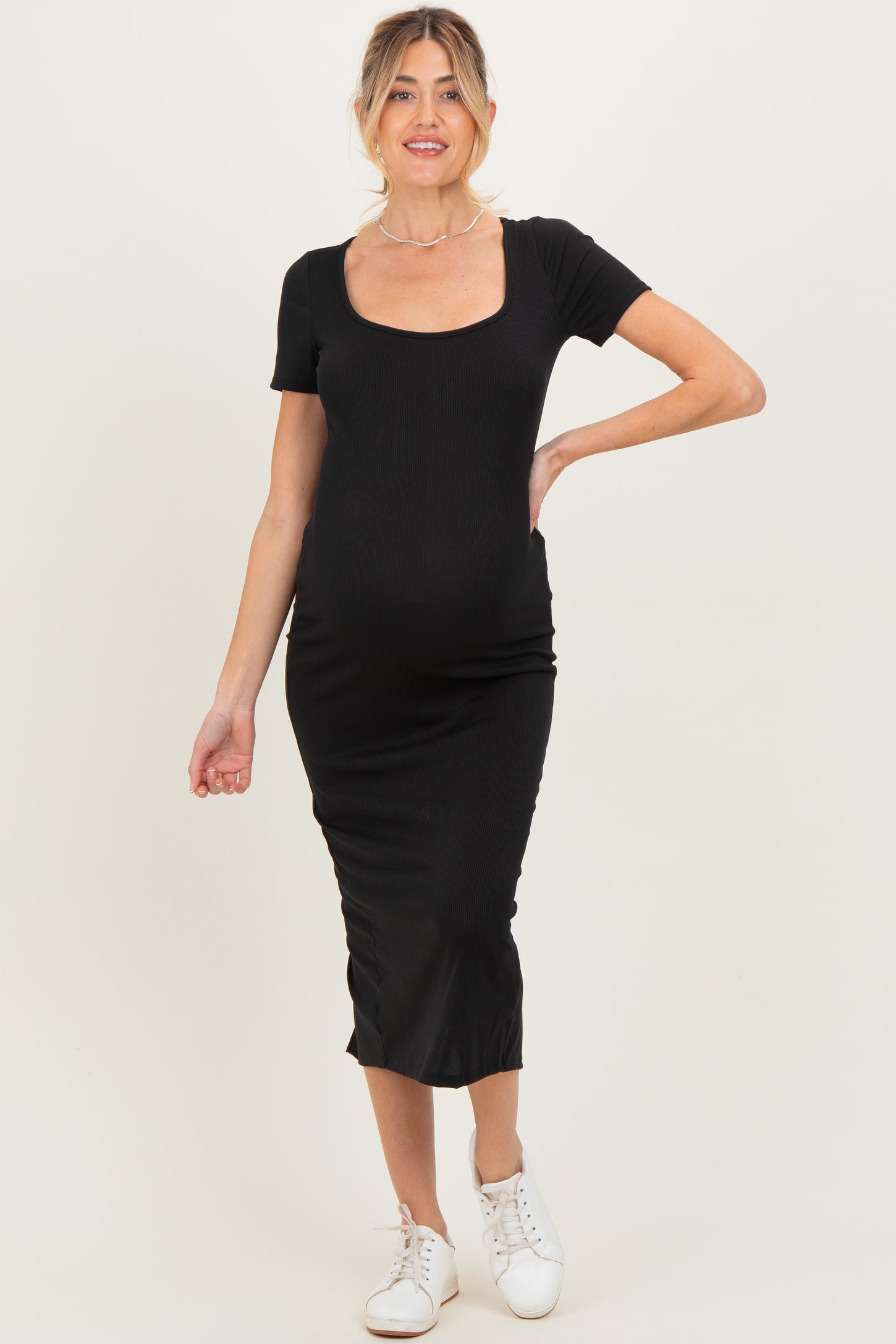 woman wearing a black ribbed maternity dress with short sleeves and a fitted silhouette, showing her baby bump