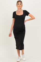 woman wearing a black ribbed maternity dress with short sleeves and a fitted silhouette, showing her baby bump