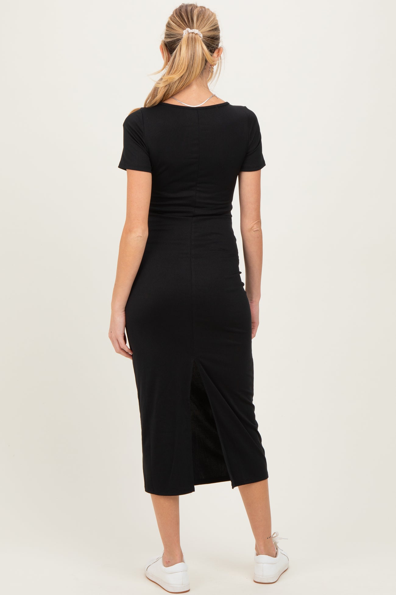 woman wearing a black maternity midi dress with short sleeves and a back slit, showing a baby bump from the side