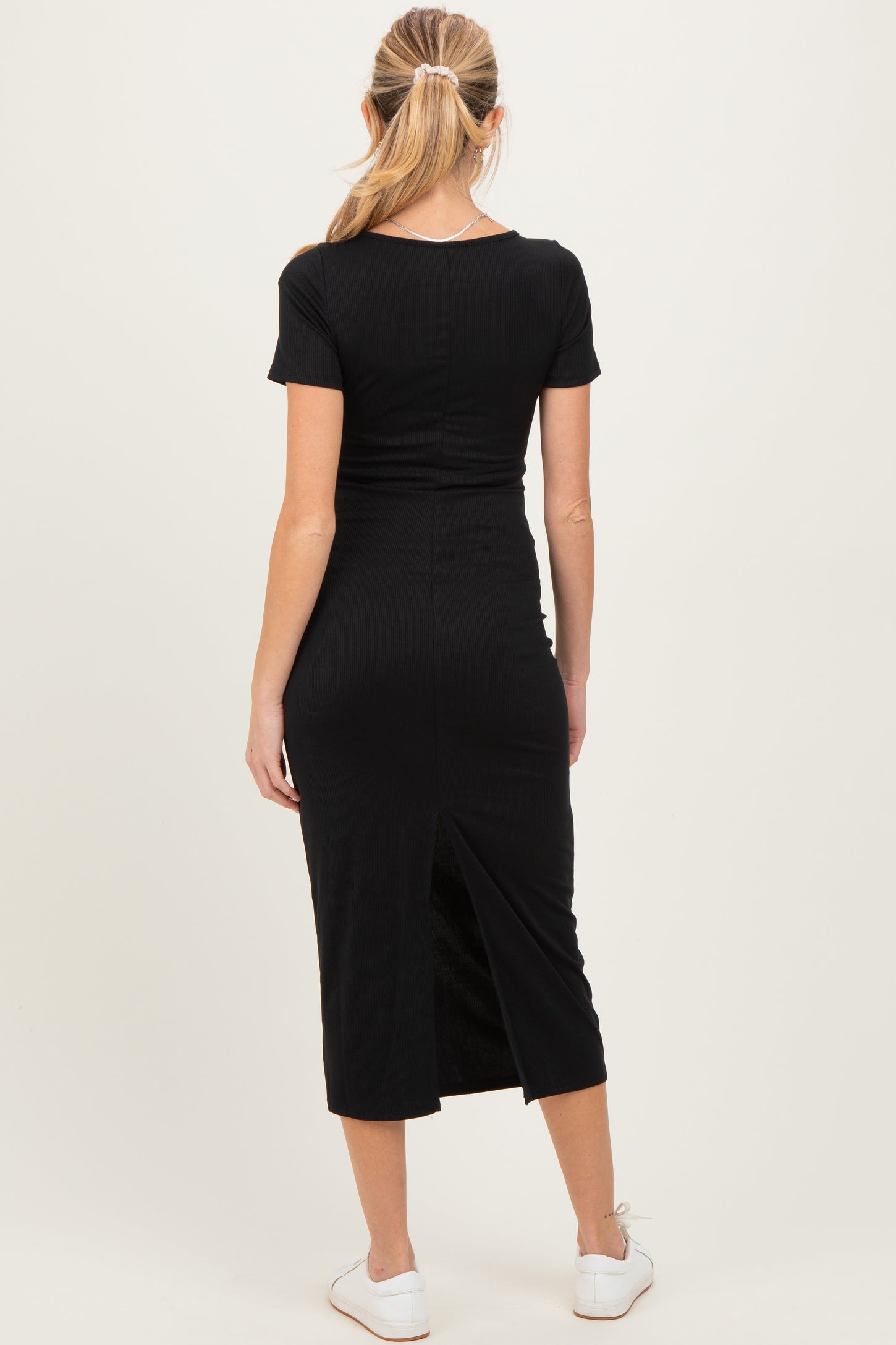 woman wearing a black maternity midi dress with short sleeves and a back slit, showing a baby bump from the side