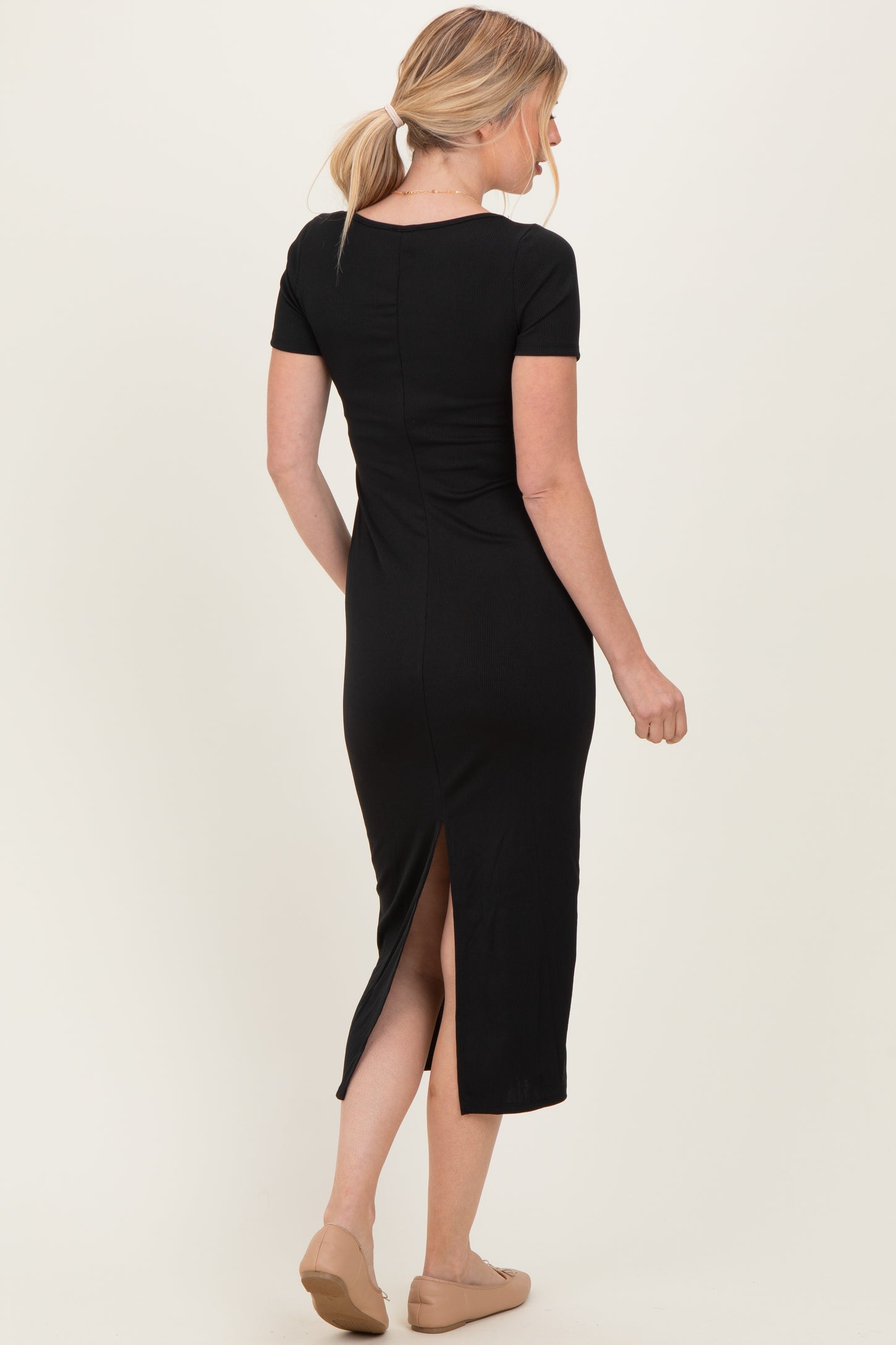 woman wearing a black ribbed midi dress with short sleeves and a back slit, viewed from the back