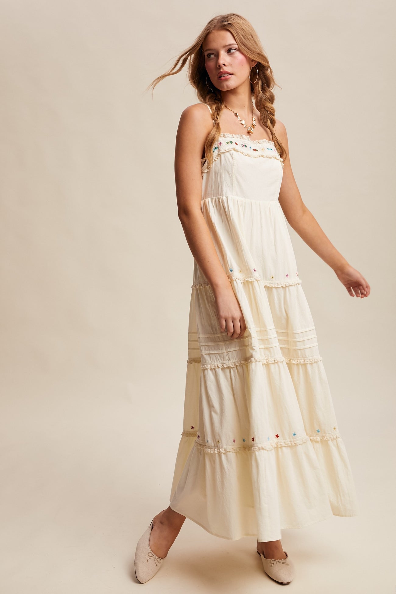 woman wearing a flowing cream maxi dress with colorful embroidery and tiered layers, styled with beige flats