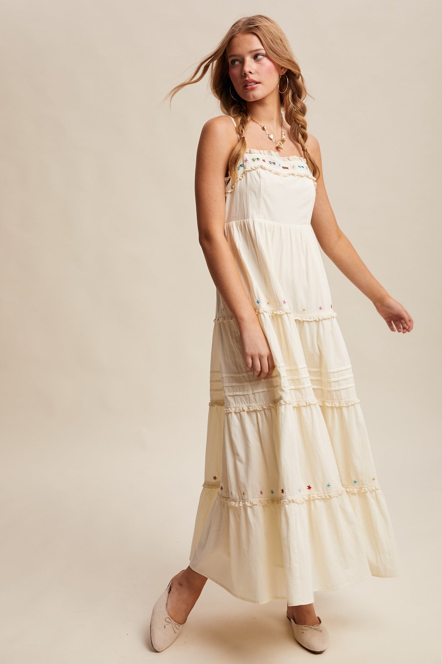 woman wearing a flowing cream maxi dress with colorful embroidery and tiered layers, styled with beige flats