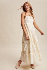 woman wearing a flowing cream maxi dress with colorful embroidery and tiered layers, styled with beige flats