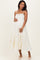 woman wearing a white tiered maternity dress with colorful embroidery and holding her baby bump