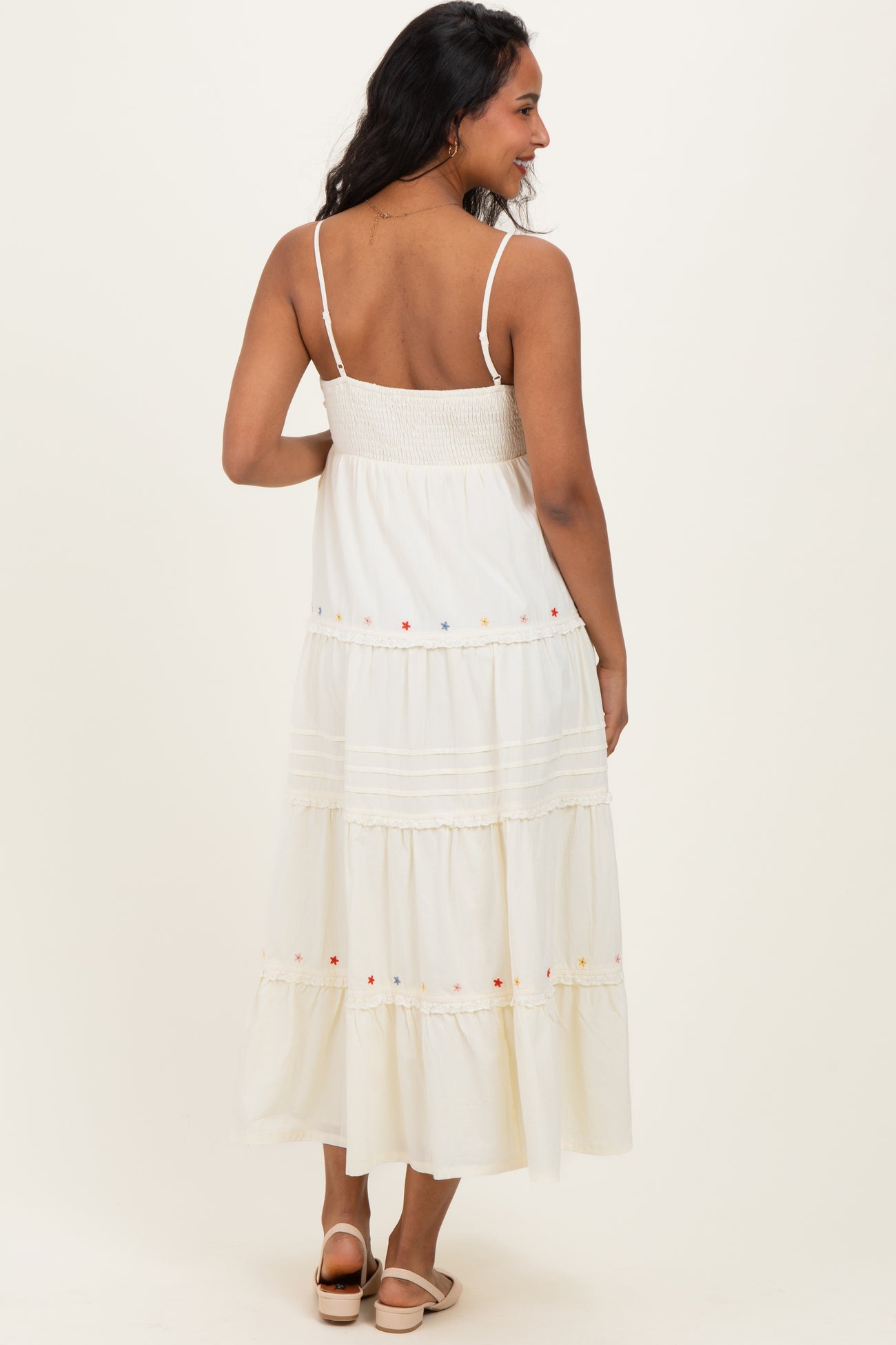 woman wearing a white maternity maxi dress with a smocked bodice and colorful embroidery on the tiers, showing her back