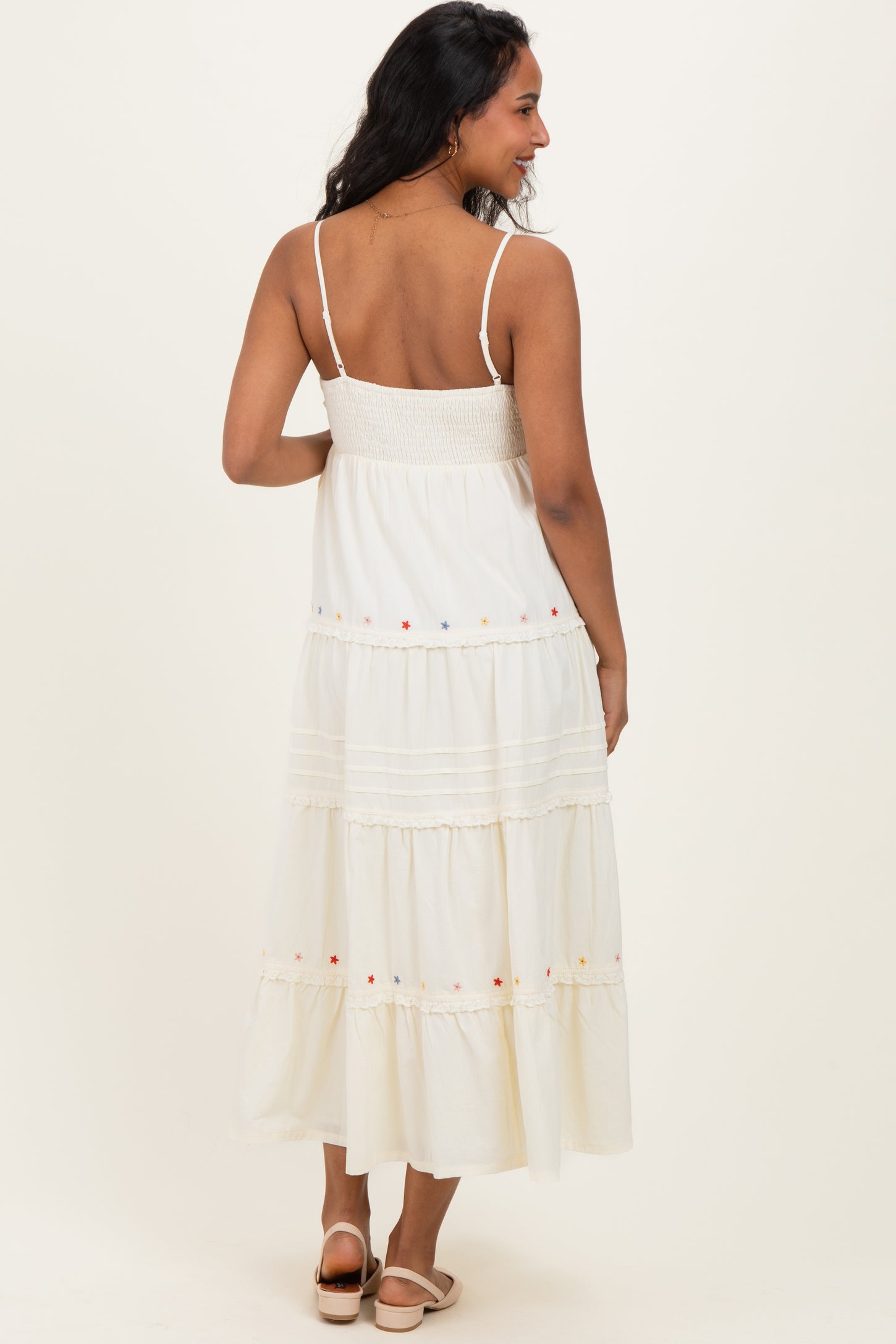 woman wearing a white maternity maxi dress with a smocked bodice and colorful embroidery on the tiers, showing her back