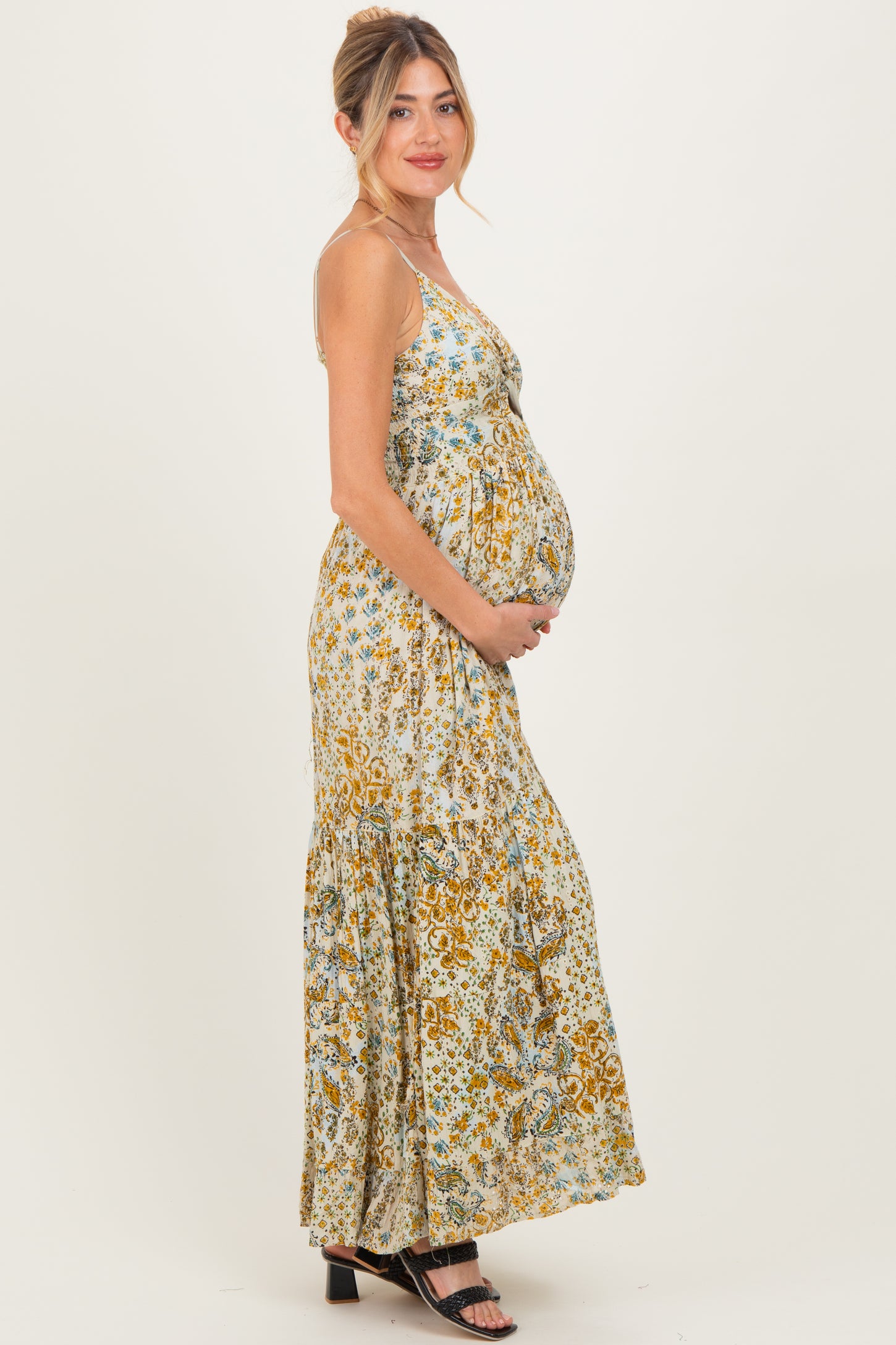 woman wearing a floral patterned maternity maxi dress, holding her baby bump, with a flowy skirt and spaghetti straps