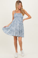 woman wearing a blue floral maternity dress with adjustable straps and a flared skirt, holding it out playfully