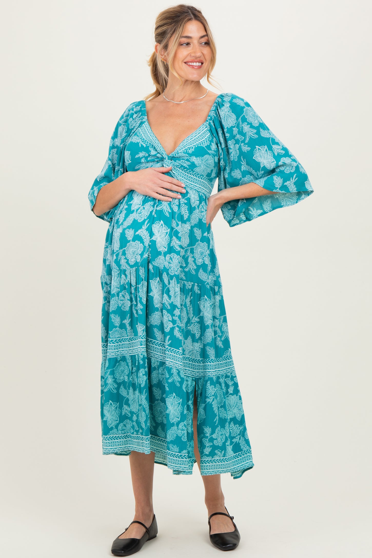 woman wearing a turquoise floral maternity dress with flowing sleeves and a baby bump visible