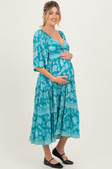 woman wearing a teal floral print maternity dress with a v-neckline and three-quarter sleeves, showing her baby bump