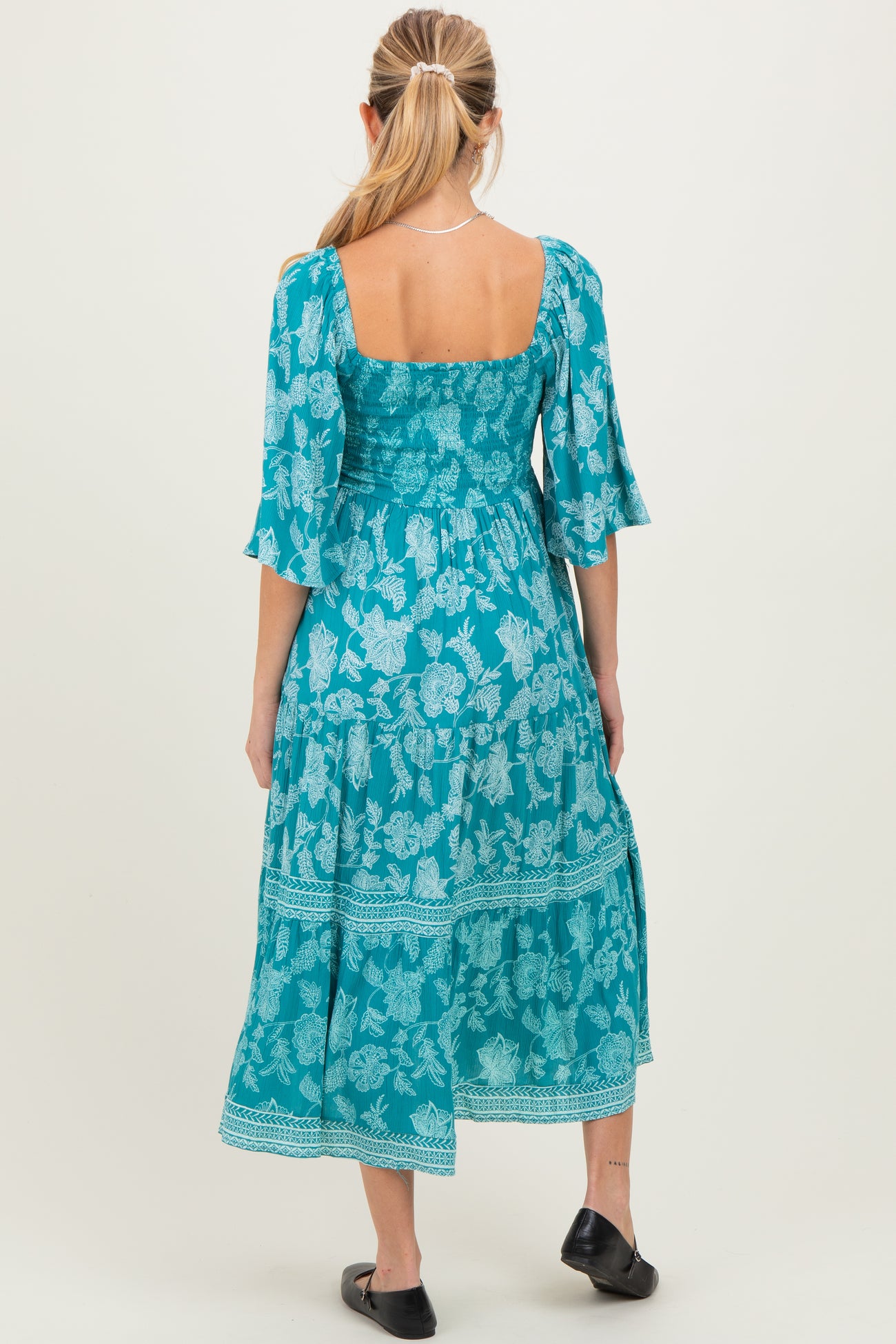 woman wearing a turquoise floral maternity maxi dress with a square back and flutter sleeves