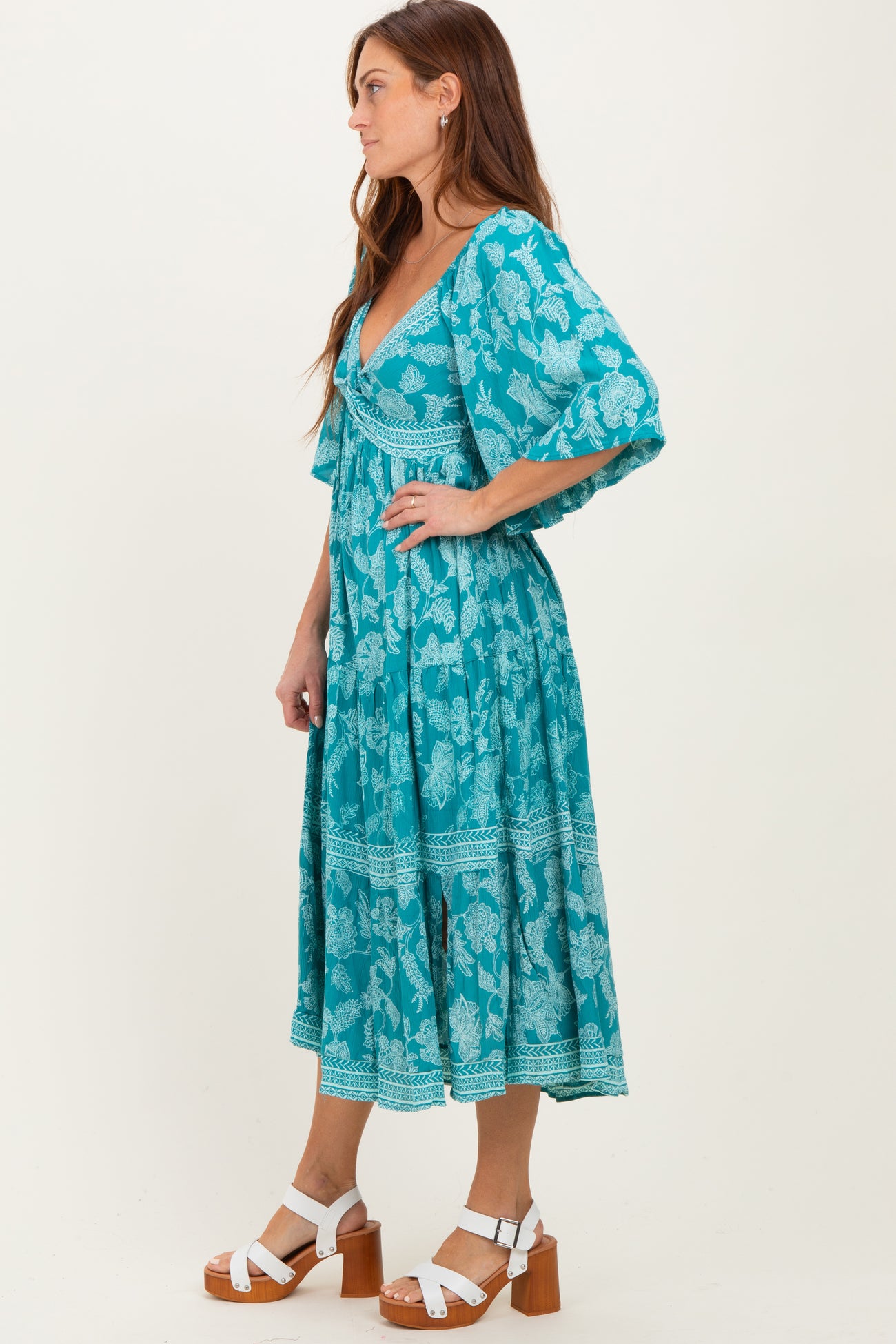 woman wearing a teal floral print midi dress with short sleeves and a flowy silhouette, paired with white sandals