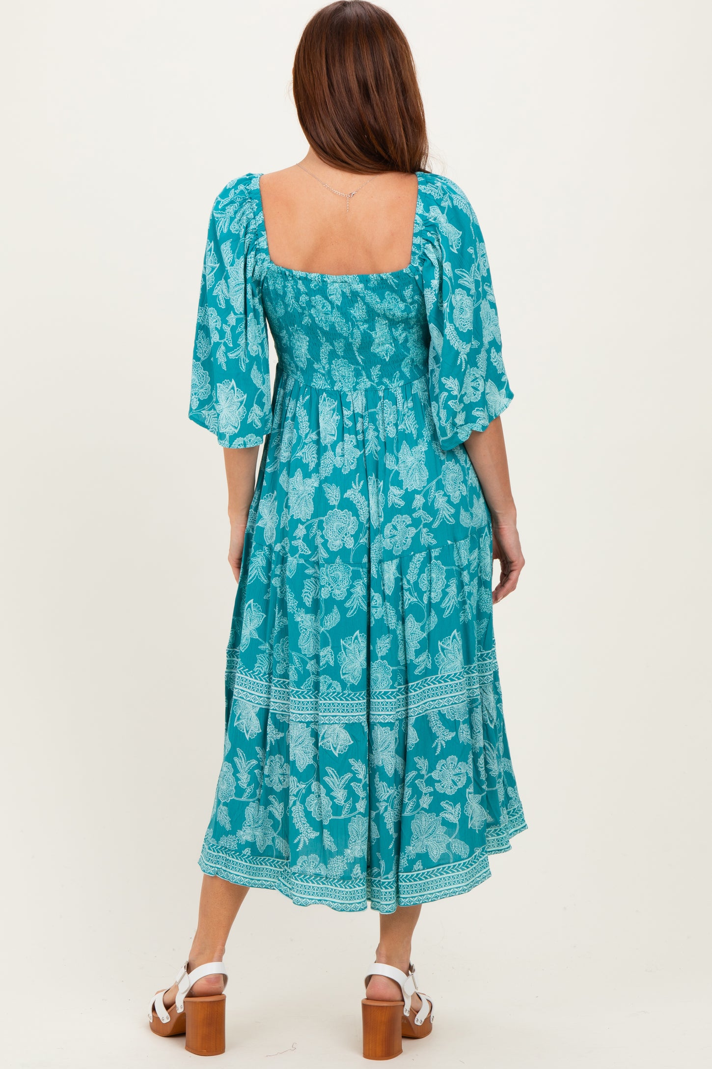 woman wearing a turquoise floral midi dress with a square neck and puffed sleeves, shown from the back