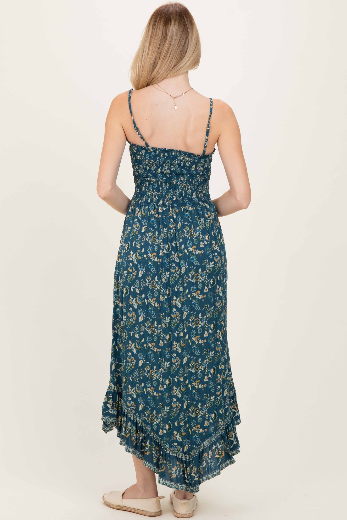 woman wearing a teal floral maxi dress with a smocked bodice and ruffled hem, viewed from the back