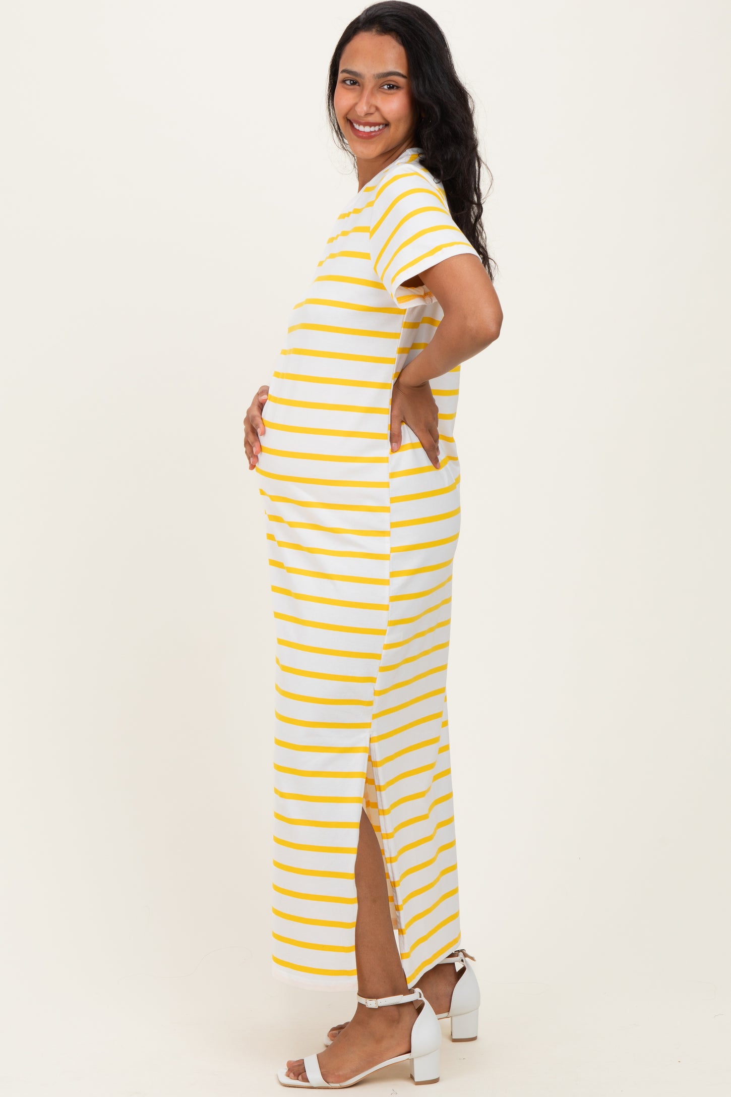 woman wearing a yellow and white striped maternity maxi dress, showing her baby bump with side slits