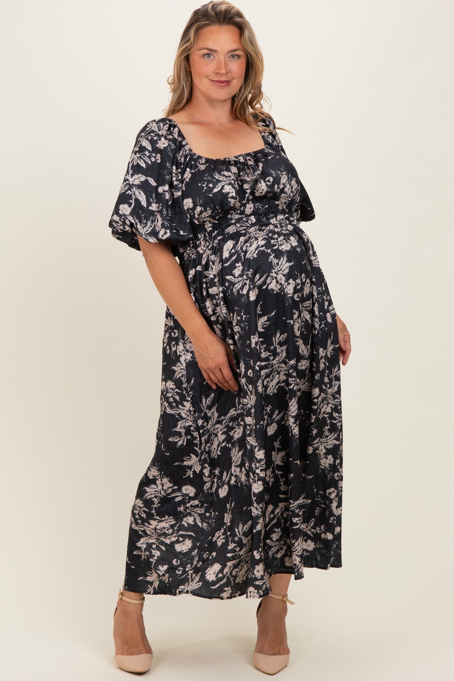 woman wearing a floral black maternity maxi dress with a square neckline and puff sleeves, holding her baby bump