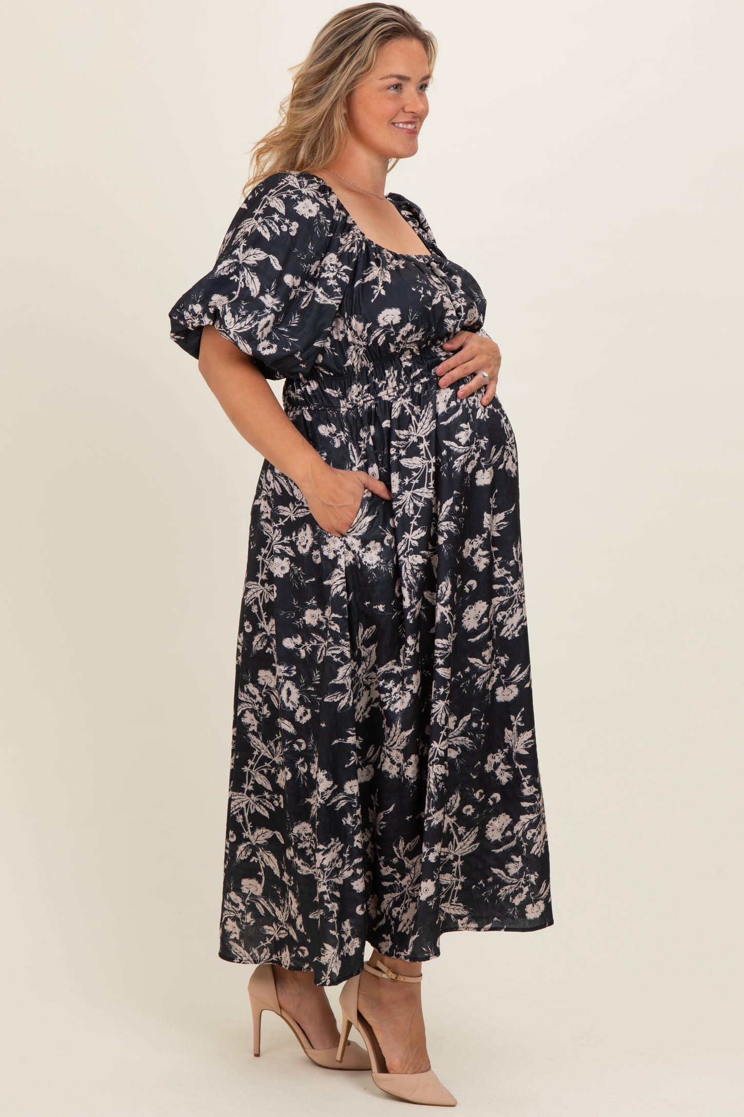 woman wearing a black floral maternity maxi dress with puff sleeves and pockets, showing her baby bump