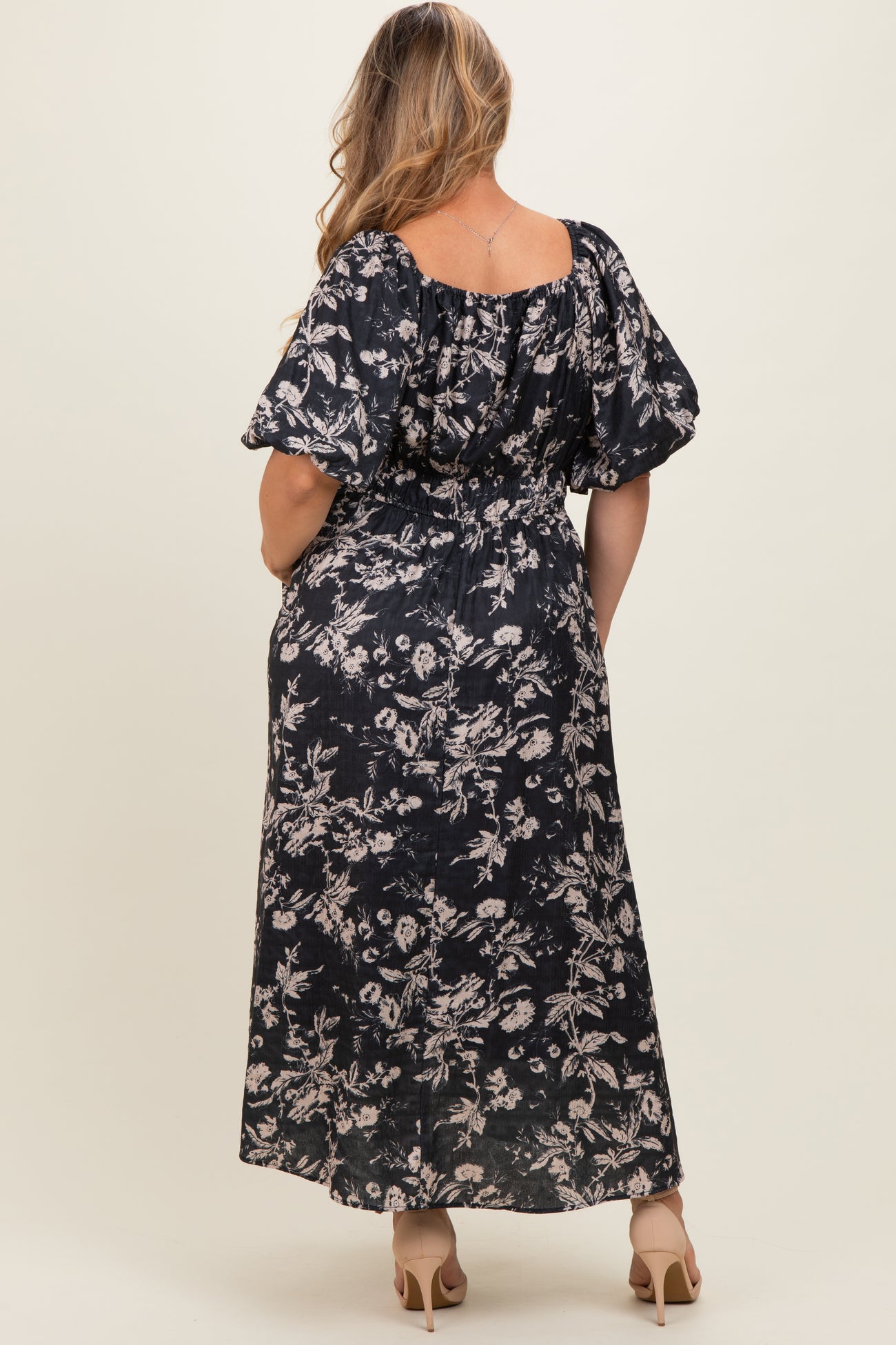 woman wearing a dark floral maternity maxi dress with puff sleeves, showing her back and long skirt