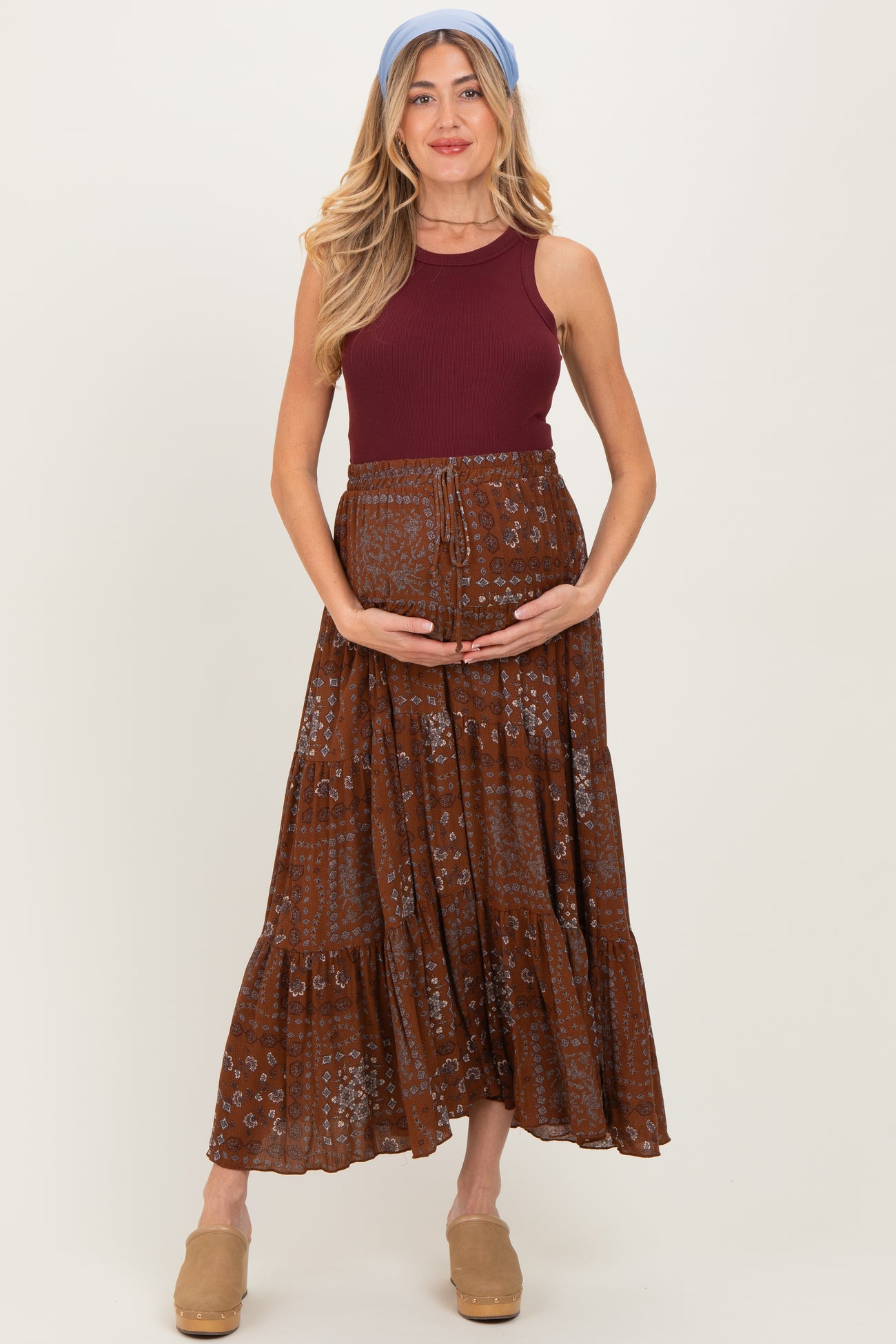 woman wearing a maroon maternity tank top and a brown floral maxi skirt, holding her baby bump