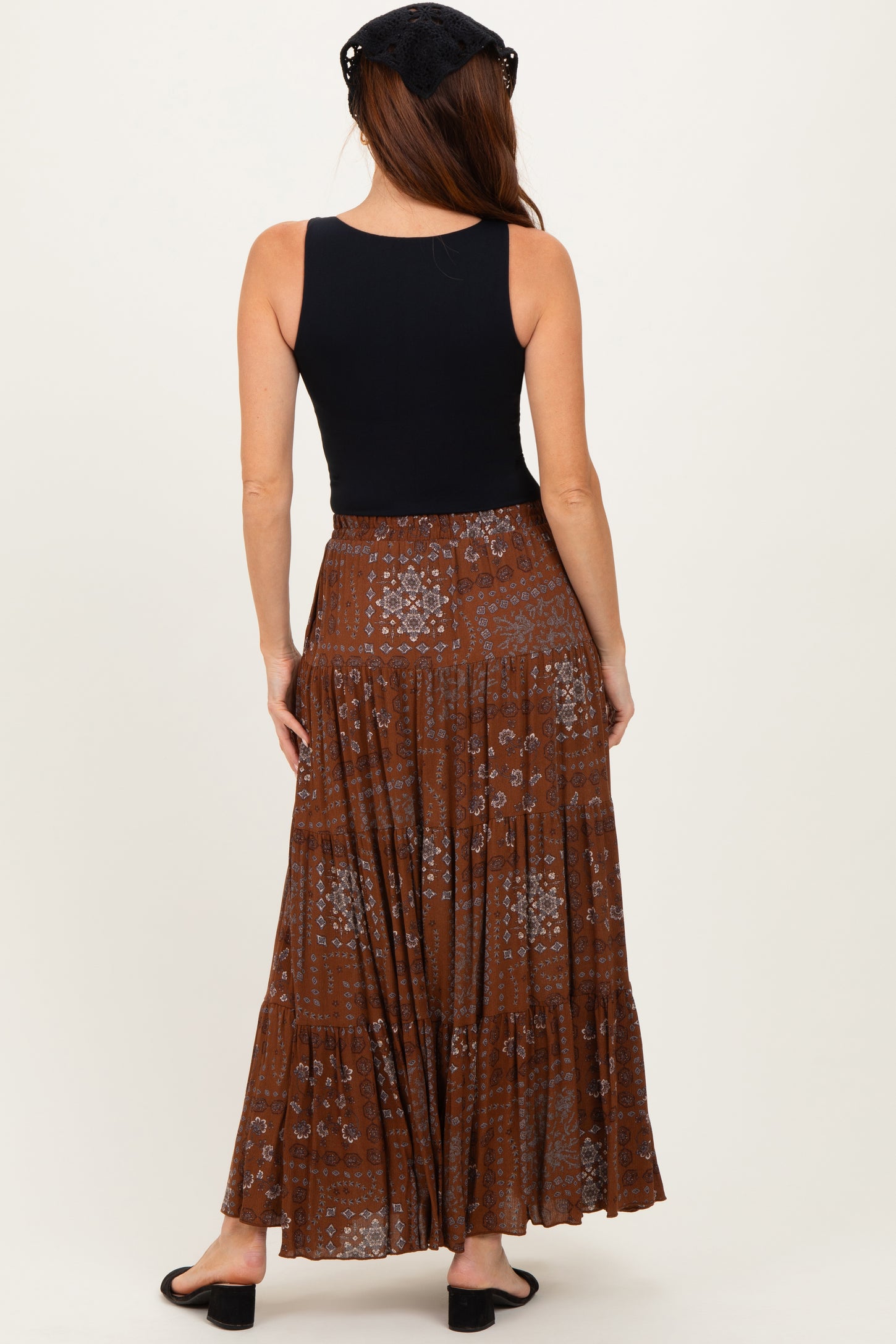 woman wearing a black sleeveless top and a long brown patterned maxi skirt, seen from the back