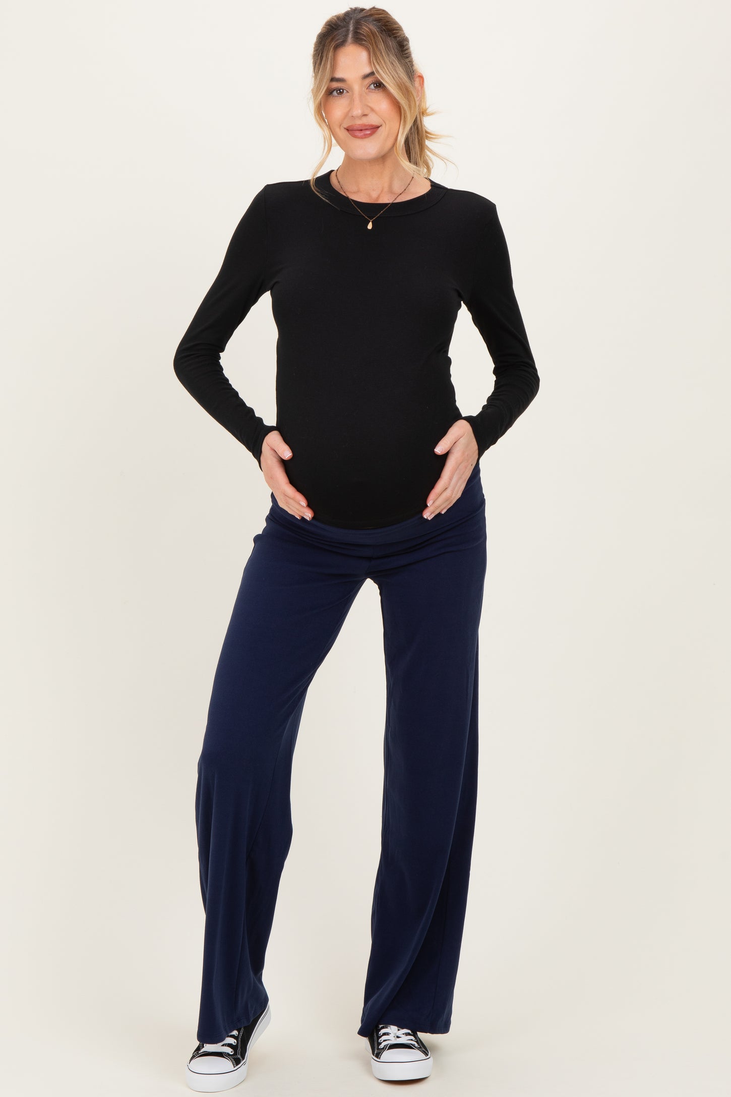 woman wearing a black long sleeve maternity top and navy wide leg maternity pants, holding her baby bump