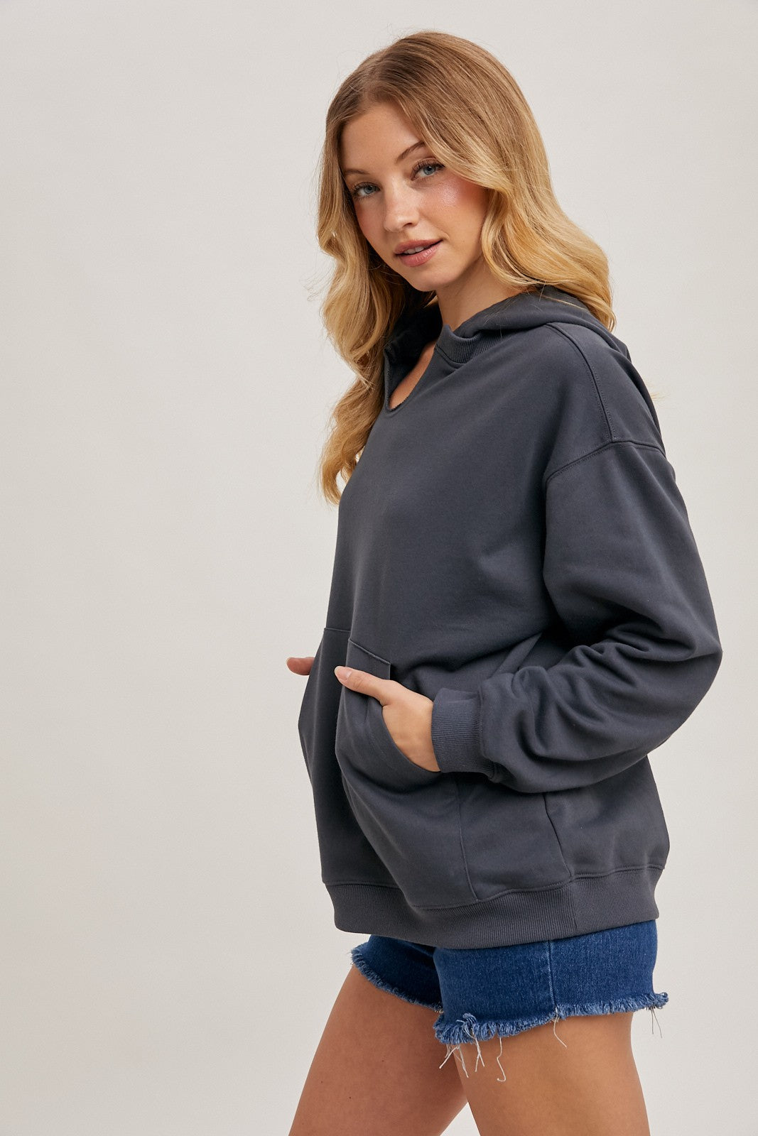 woman wearing a charcoal grey oversized hoodie with a front pocket and paired with denim shorts