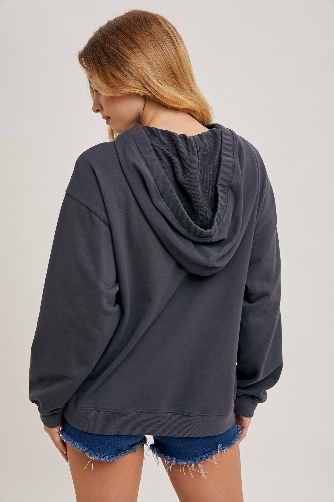 woman wearing a dark gray hooded sweatshirt with a relaxed fit and back view, paired with denim shorts