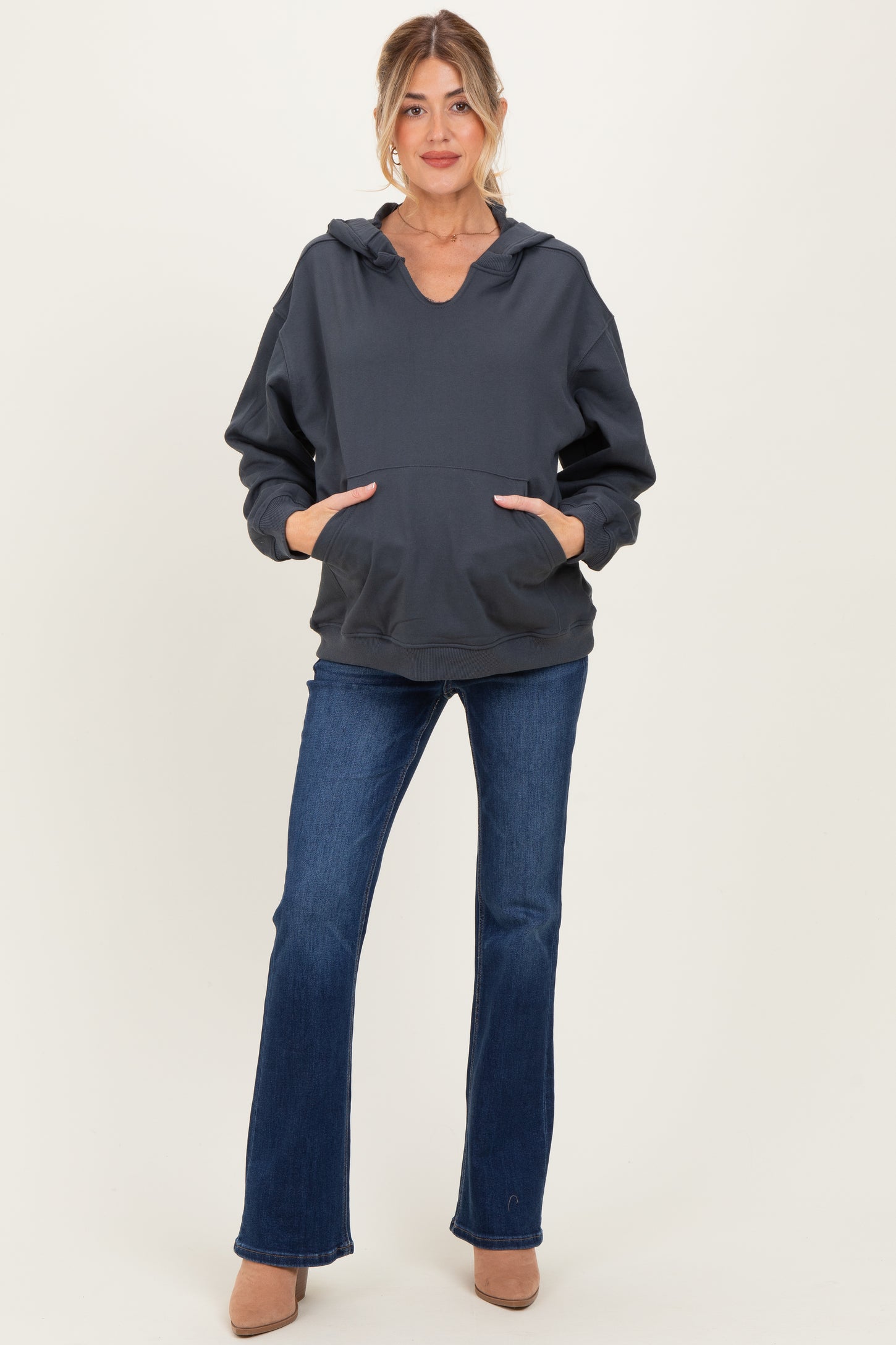 woman wearing a dark gray maternity hoodie with a v-neck and front pockets paired with flared jeans