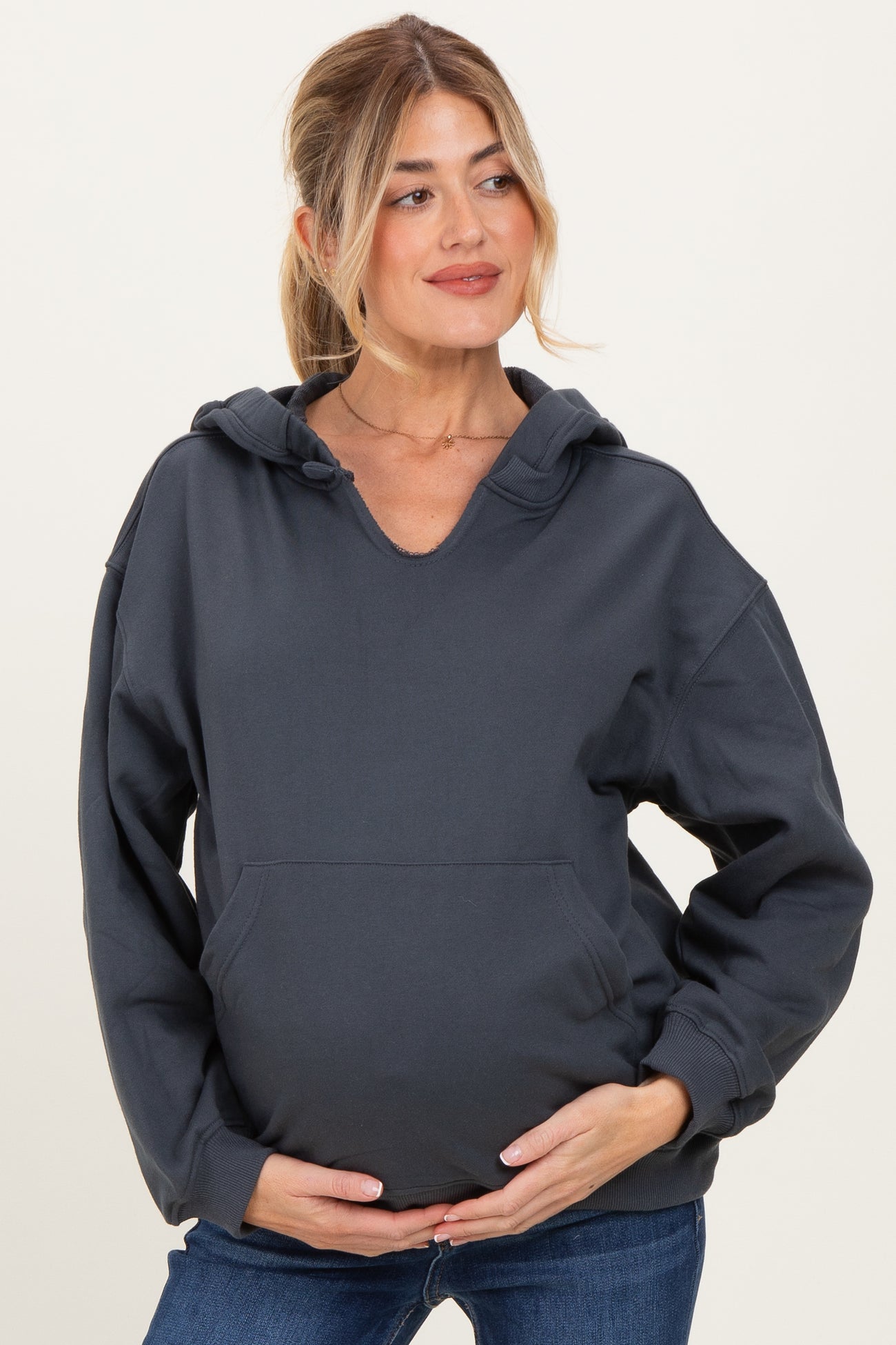 woman wearing a charcoal gray maternity hoodie with a v-neck and kangaroo pocket, holding her baby bump