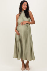 woman wearing a sage green pleated maternity dress, showcasing her baby bump with a smiling pose