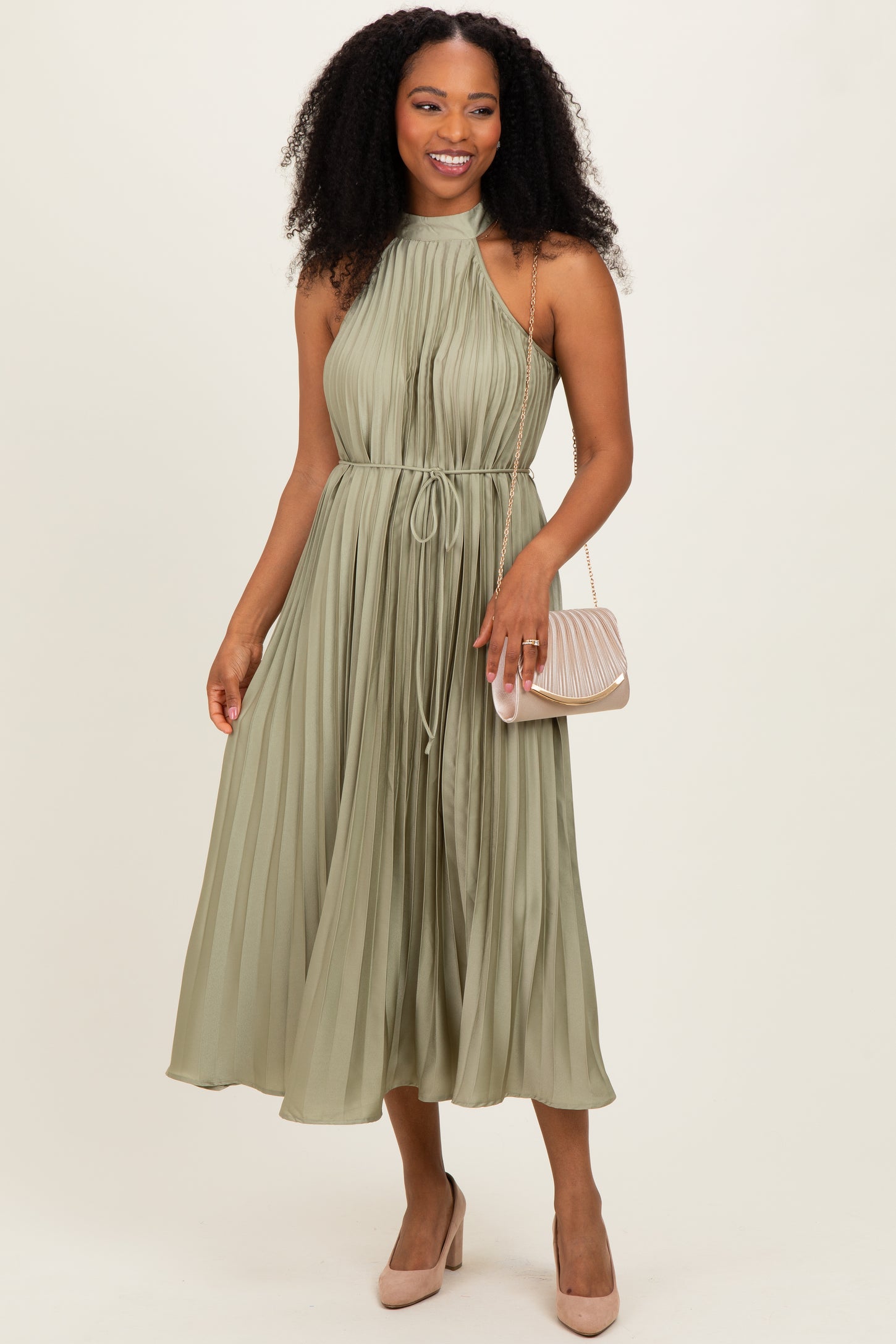 woman wearing a sage green pleated halter dress with a drawstring waist and holding a small handbag