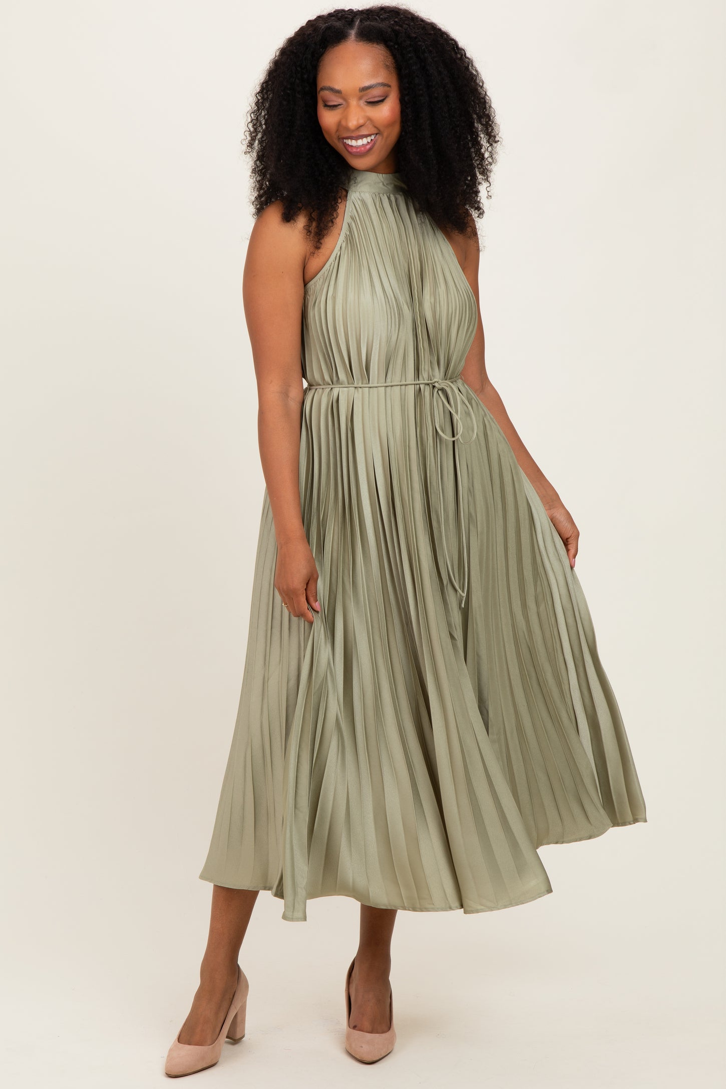 woman wearing an olive green pleated midi dress with a halter neck and a tie waist, standing and smiling