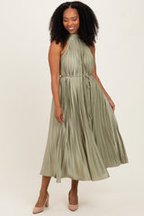 woman wearing an olive green pleated midi dress with a halter neck and a tie waist, standing and smiling