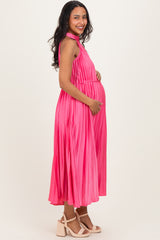 woman wearing a pink pleated maternity dress and cradling her baby bump