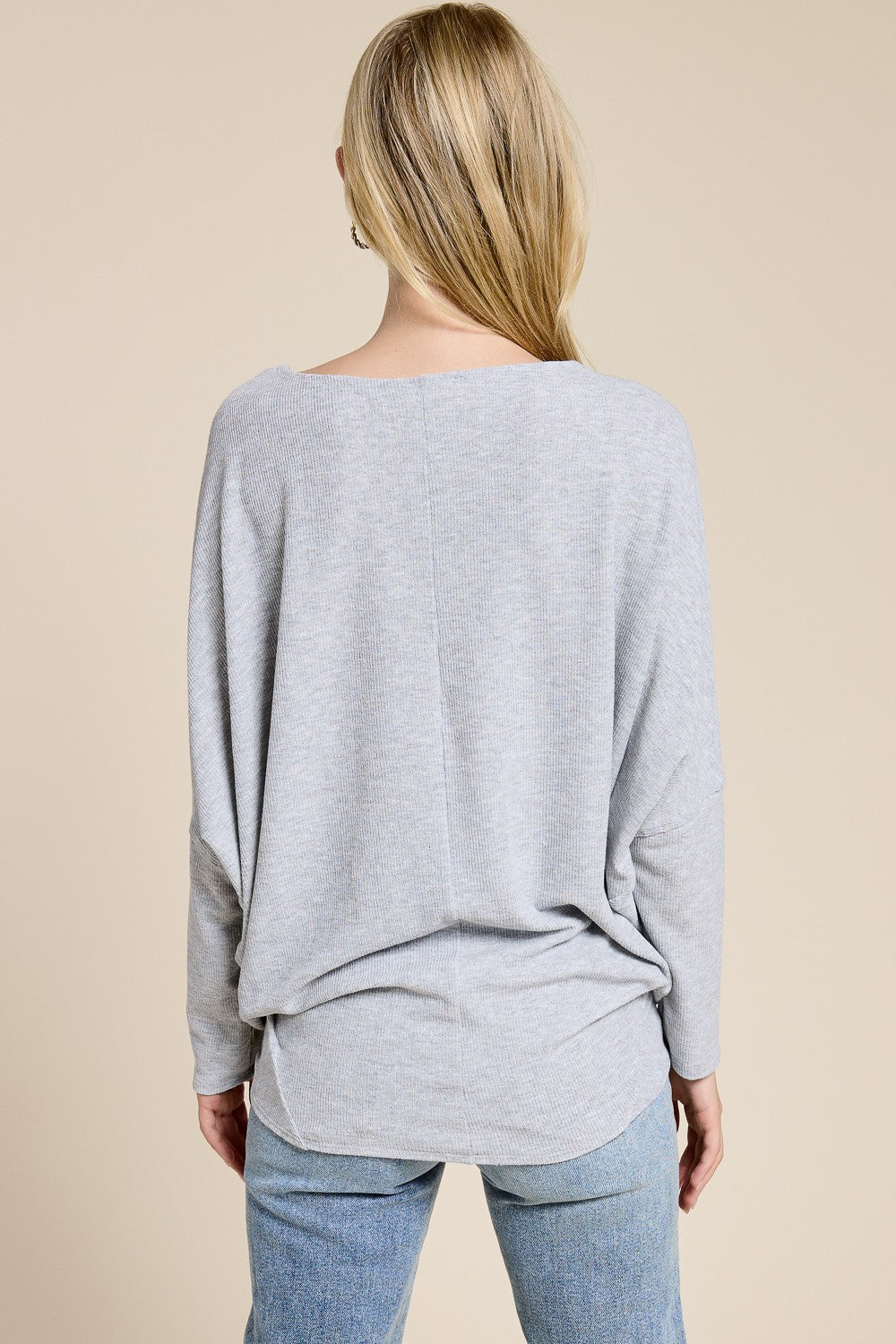woman wearing a relaxed fit gray long sleeve top with a scoop back and side slits, paired with light blue jeans