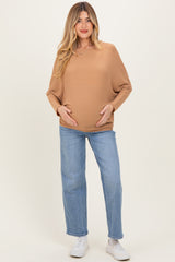 woman wearing a brown knit maternity sweater and blue jeans, showing her baby bump