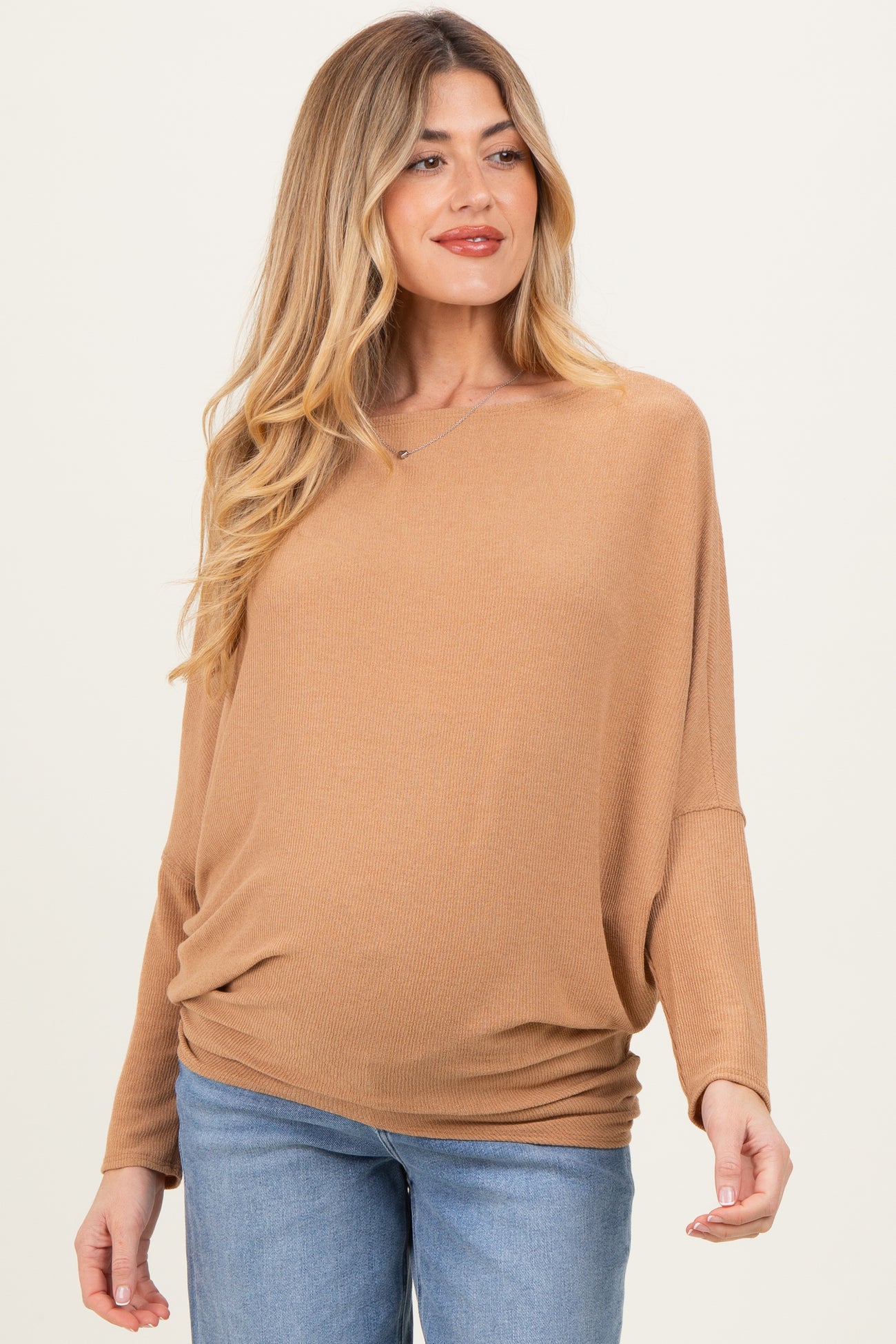 woman wearing a light brown maternity top with a relaxed fit and long sleeves, showcasing her baby bump